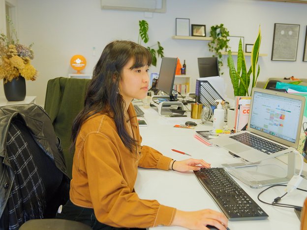 A young professional sits at their desk using a computer. They are in a modern office space.