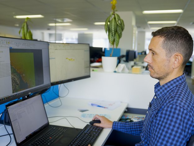 A male looks at a computer screen and sits at a desk.