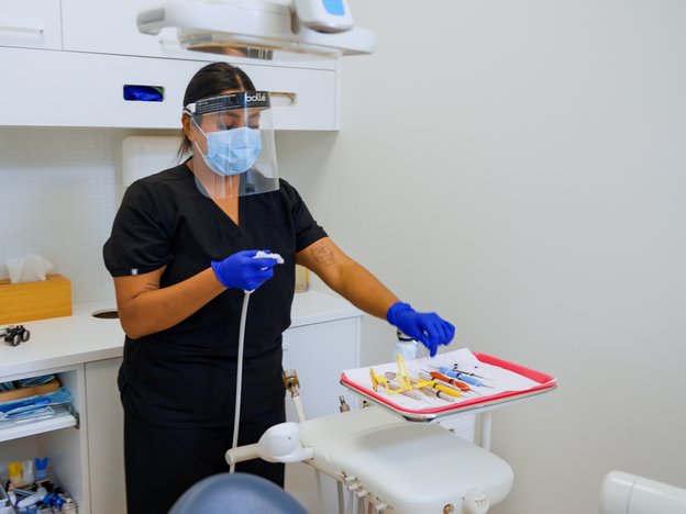 An oral health therapist is wearing a mask and using tools in a dental surgery.