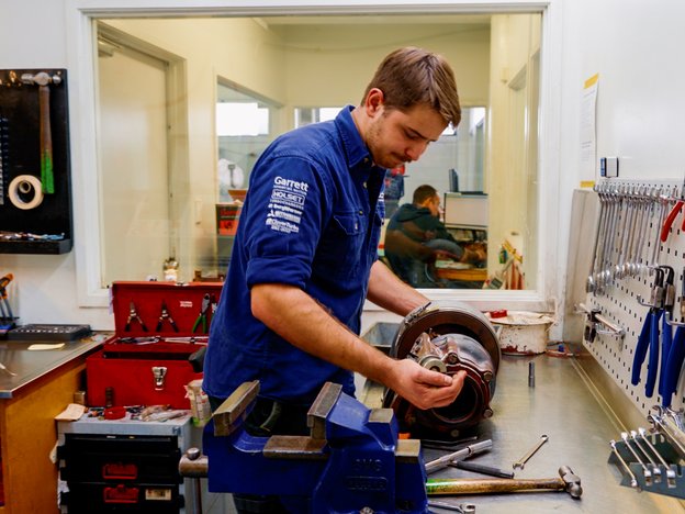 A man in a blue shirt works at a workbench with tools.