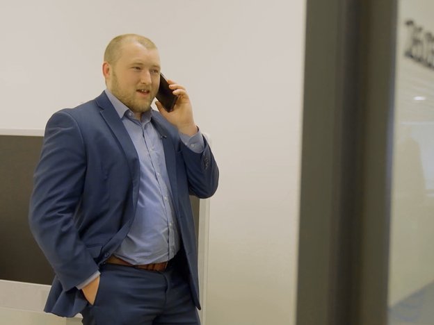 A man holds a mobile phone to his ear. He speaks into it. He wears a dark blue suit.