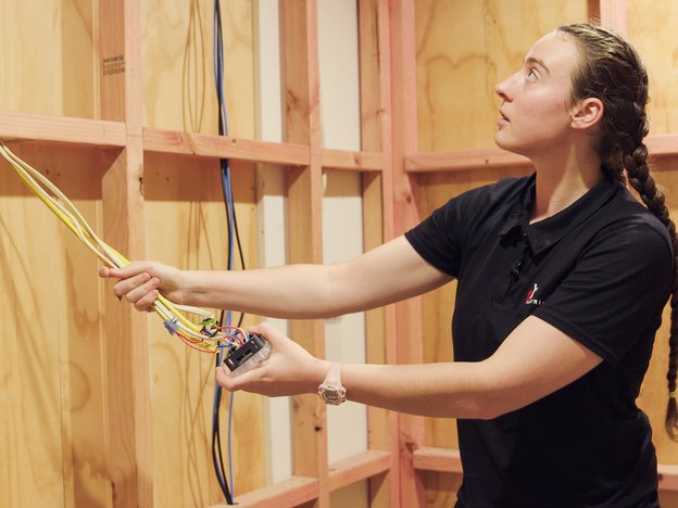 A young woman stands inside a building frame holding onto electrical wires.