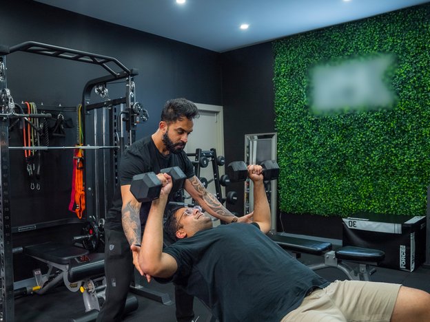 A male lifts weights and another male helps.