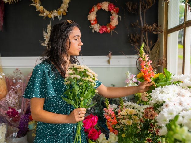 A young woman picks flowers in a store. She is surrounded by a variety of flowers.