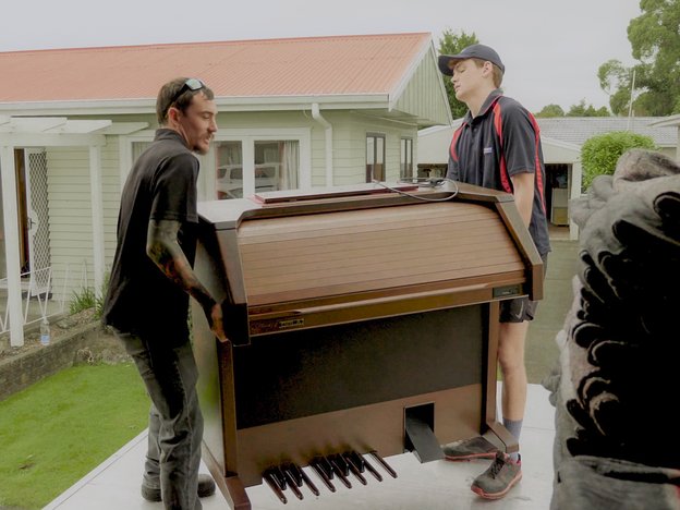 Two males carry a piano out of a storage truck.