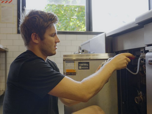 A man uses a screwdriver to fix a dishwasher in a kitchen.