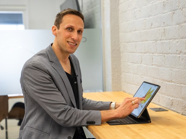 A man uses his finger on a touch screen laptop. He sits at a desk in an office.