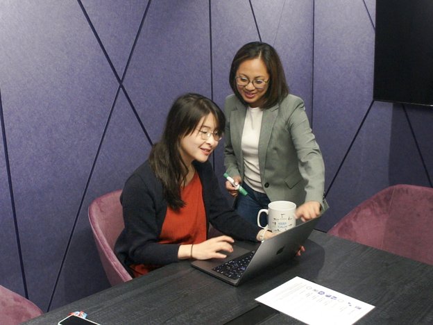Two females look at a computer screen and smile.