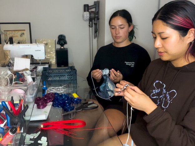 Two woman stand making jewellery with their hands in a workshop.