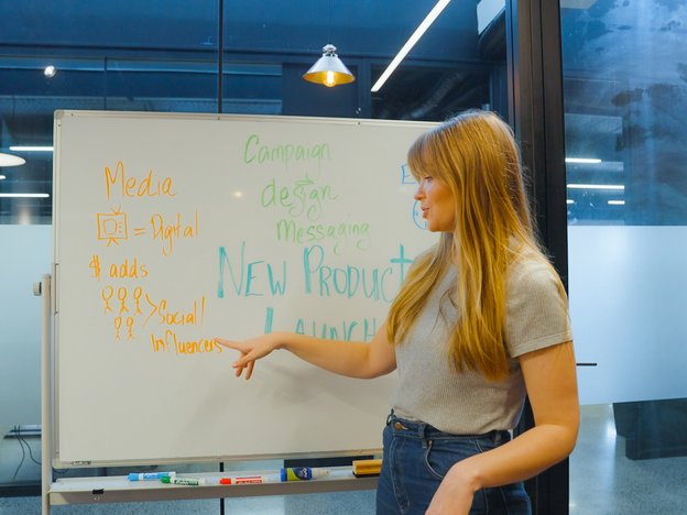 A woman stands pointing at words written on a whiteboard in a meeting room.