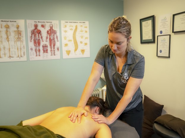 A massage therapist gives a client a massage. Their client is laying face down on the table while they massage their back.
