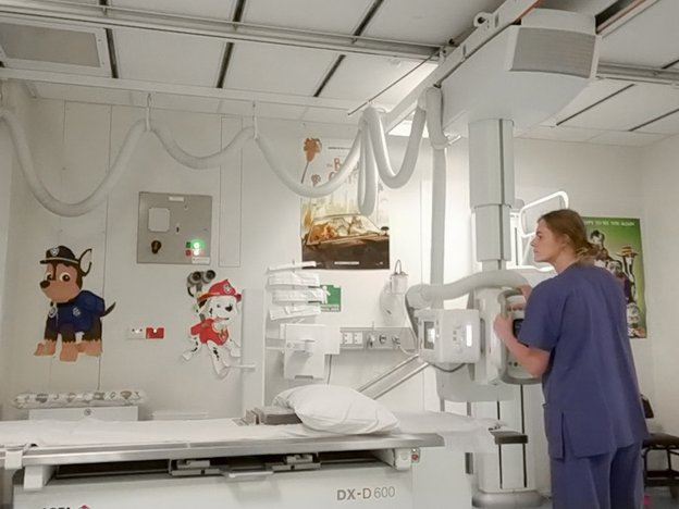 A woman wears a medical uniform and checks a medical imaging machine.
