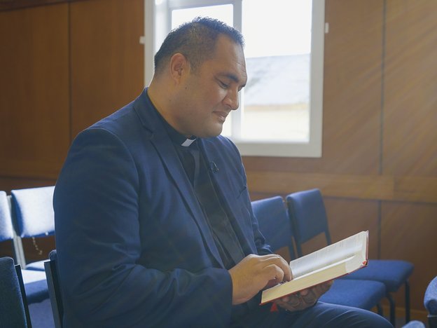 A person in a church reads a book. They are in formal wear and light shines through the window behind them.