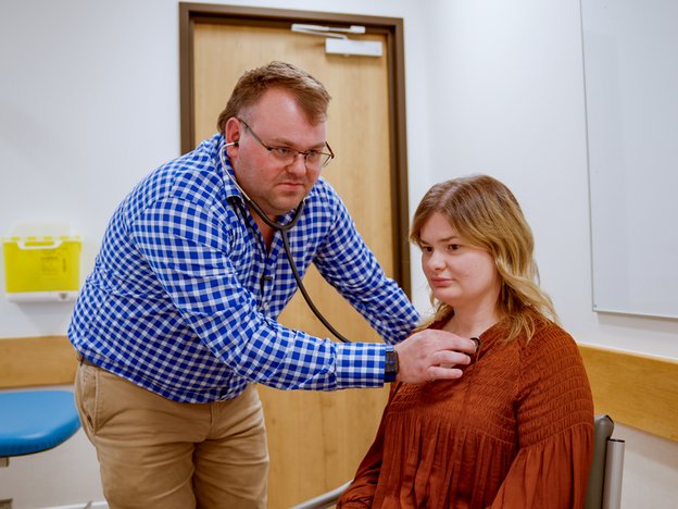 A nurse practitioner is listening to a patient's chest with a stethoscope.