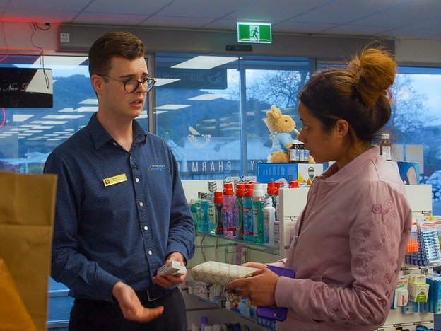 A male pharmacist assists a patient in a pharmacy.