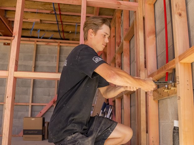 A young man tightens some pipes in the wall of a concrete building.