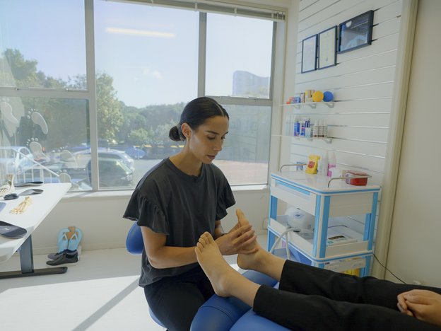 A podiatrist massages the feet of a patient. They are in a sunny clinic room.