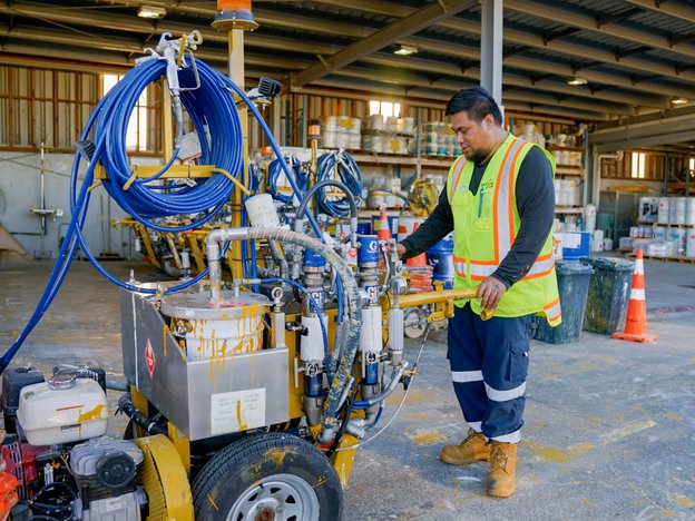 Road marker wearing hi-vis is operating a line painting machine.