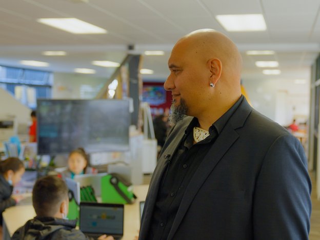 A school principal observes classroom. Children can be seen using computers behind them.
