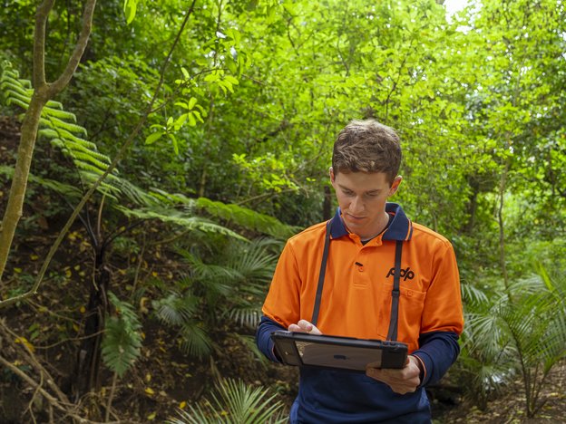 A young man in the bush holding an iPad.