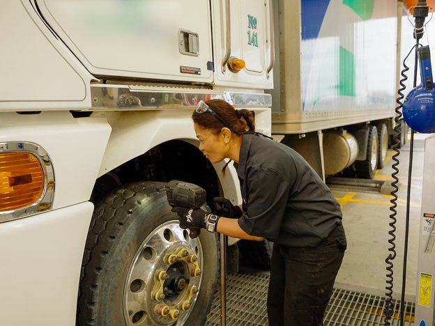A person checks the tyre of a truck. They are wearing black overalls.
