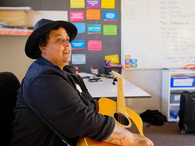 E noho ana he wahine i tētahi tūru e mau kitā ana, ā, kei roto ia i tētahi akomanga.