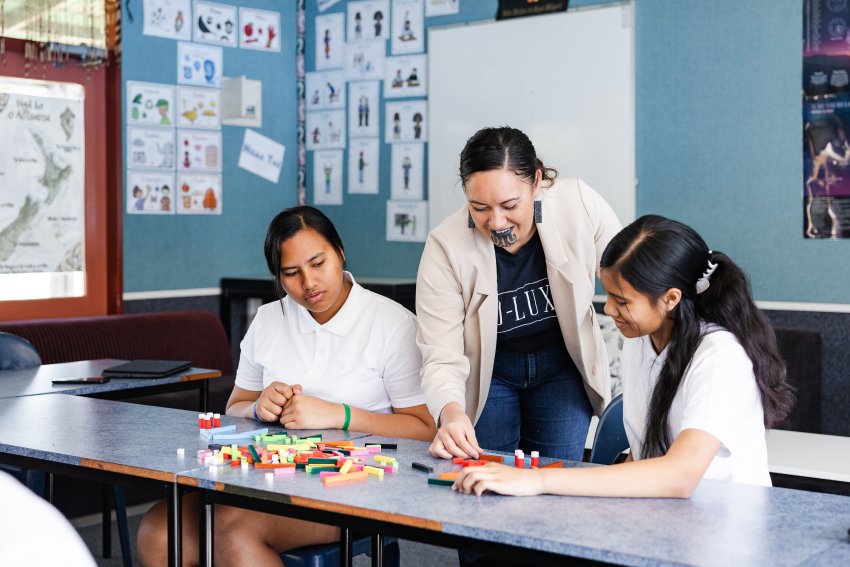 A female teacher helps two students in a classroom.
