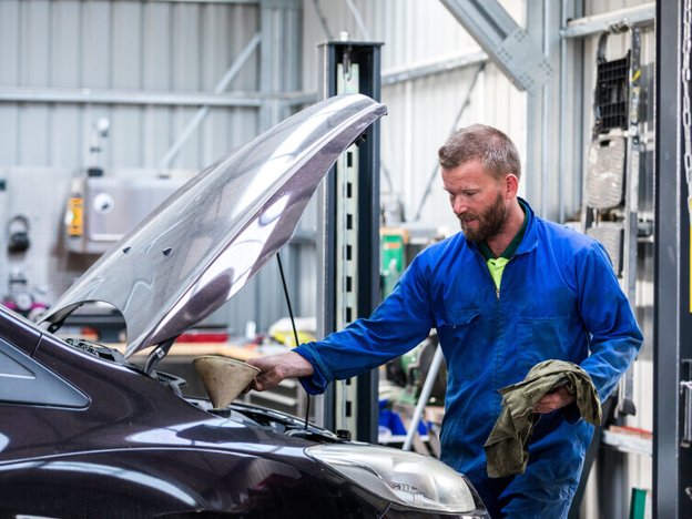 A man fills a car with oil in a mechanic's workshop.
