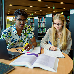 A young man and young woman study books together in a library.