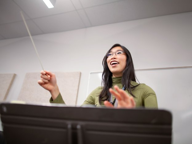 Portrait view of band instructor teacher conductor hands leading music performance orchestra of junior high school teenager students practicing in school classroom together