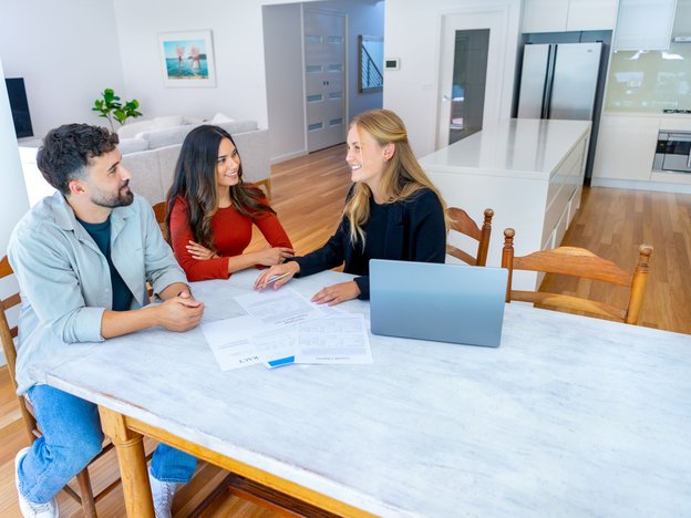 Real estate sales personal sitting across a table from two clients in an office.