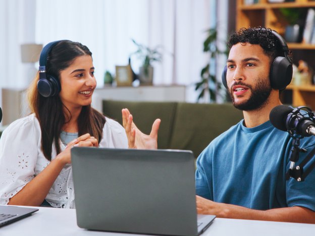 Two people record their podcast using a microphone and laptop.